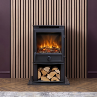 Black freestanding stove with fire burning inside, surrounded by stacked logs against a striped wall.